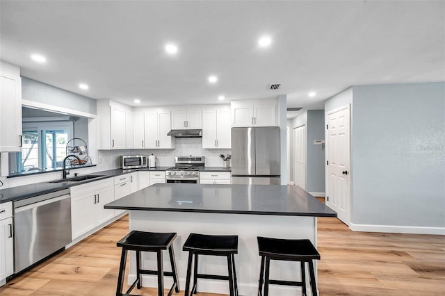 kitchen with stainless steel appliances, white cabinetry, a kitchen island, and a kitchen bar