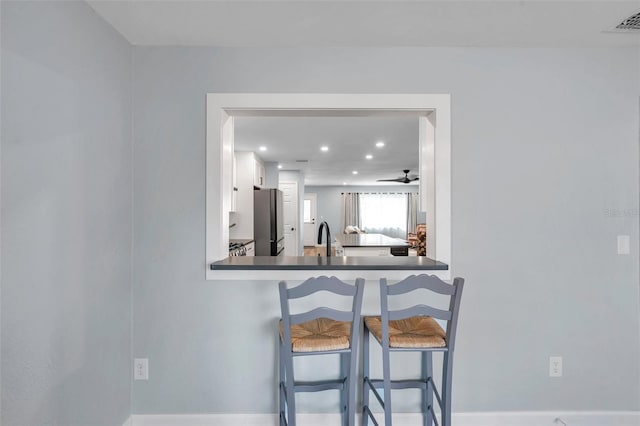 kitchen featuring sink, a breakfast bar area, stainless steel refrigerator, kitchen peninsula, and white cabinets