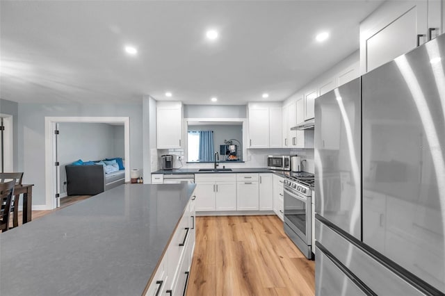 kitchen featuring appliances with stainless steel finishes, white cabinetry, sink, decorative backsplash, and light hardwood / wood-style flooring