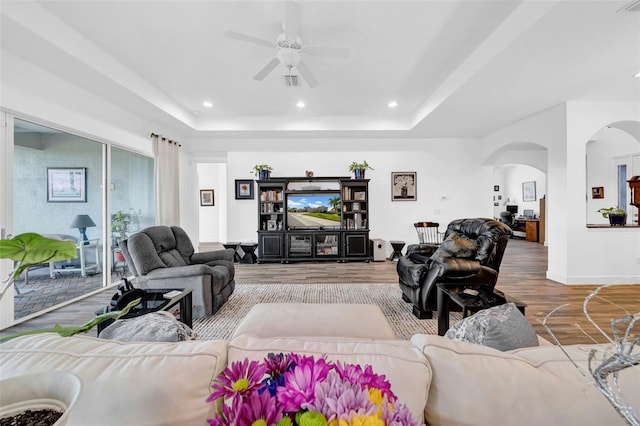 living room featuring ceiling fan, wood-type flooring, and a raised ceiling