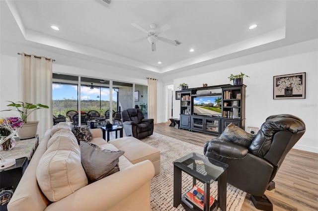 living room with ceiling fan, light hardwood / wood-style floors, and a tray ceiling