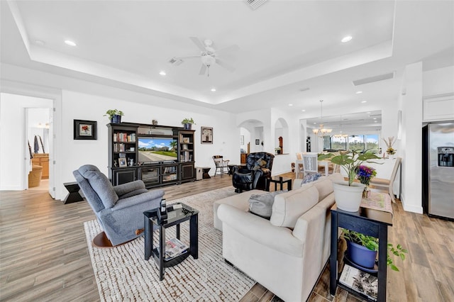 living room featuring ceiling fan with notable chandelier, light hardwood / wood-style floors, and a raised ceiling