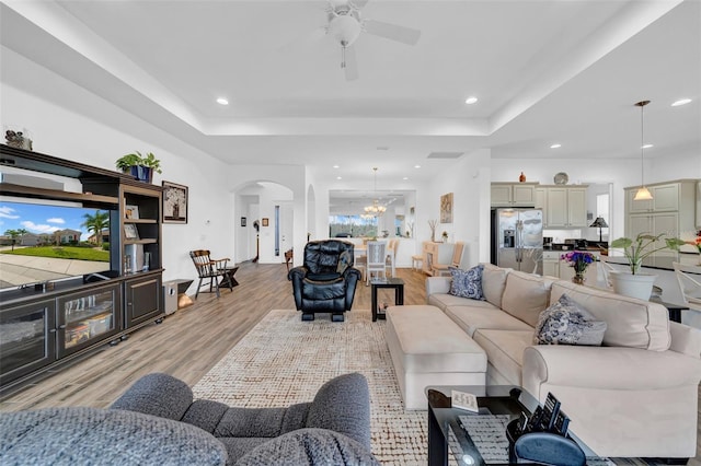 living room with a tray ceiling, ceiling fan with notable chandelier, and light hardwood / wood-style floors