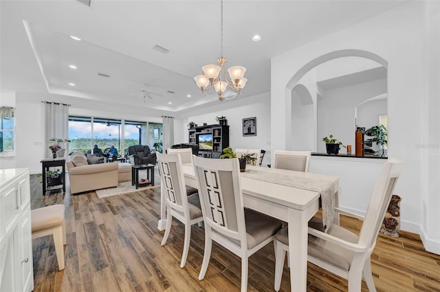 dining space with ceiling fan with notable chandelier, a raised ceiling, and light hardwood / wood-style floors