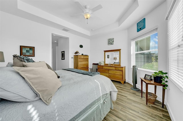 bedroom with ceiling fan, a tray ceiling, and light hardwood / wood-style flooring