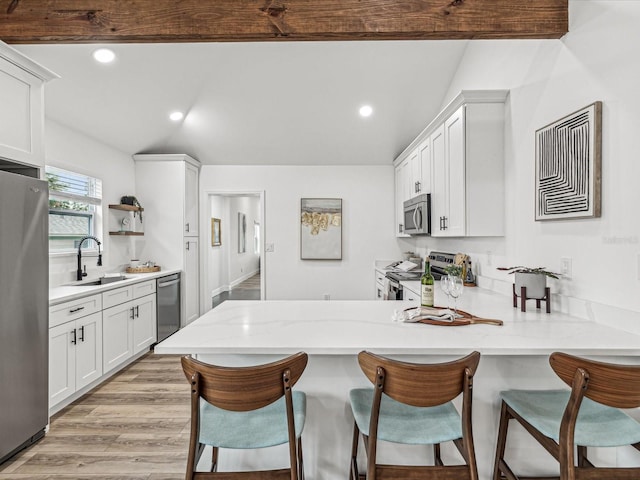 kitchen featuring sink, appliances with stainless steel finishes, white cabinetry, a kitchen bar, and kitchen peninsula