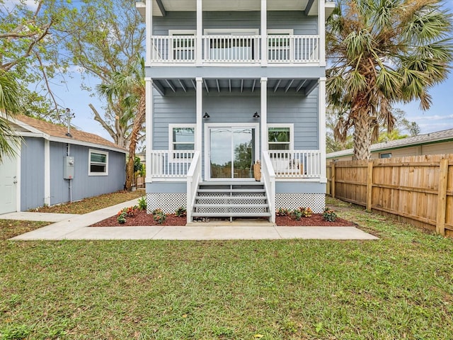 rear view of property featuring a balcony, a yard, and covered porch