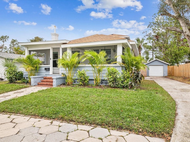 bungalow with an outbuilding, a garage, a front lawn, and a sunroom