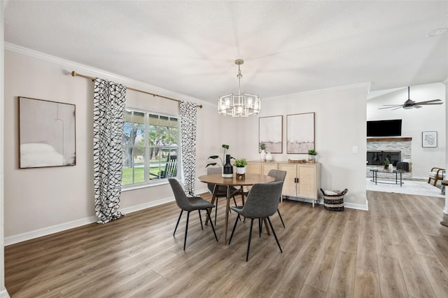 dining space with a fireplace, crown molding, wood-type flooring, and ceiling fan with notable chandelier