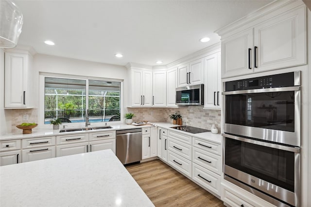 kitchen with sink, white cabinets, decorative backsplash, light hardwood / wood-style floors, and stainless steel appliances