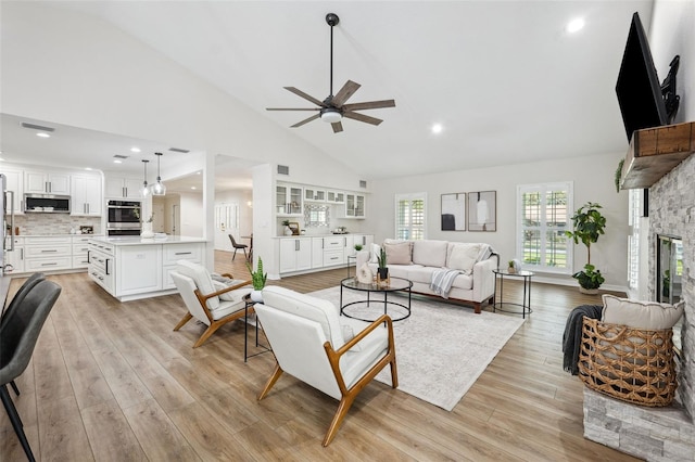 living room featuring ceiling fan, a fireplace, high vaulted ceiling, and light hardwood / wood-style flooring