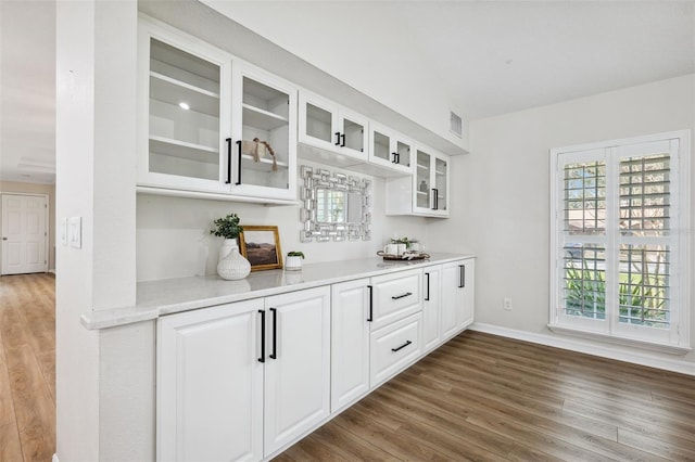 bar with white cabinetry, light stone counters, a wealth of natural light, and dark hardwood / wood-style flooring