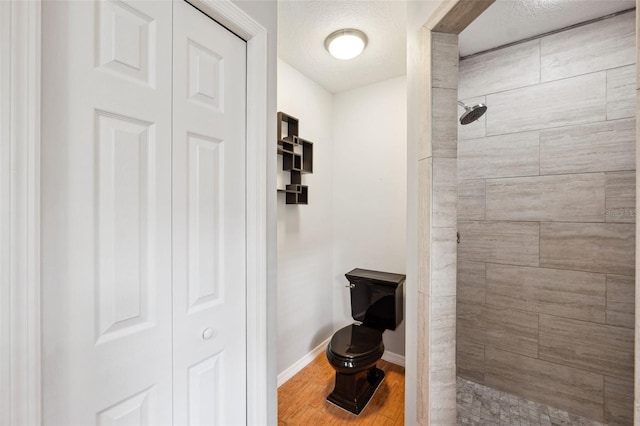 bathroom with hardwood / wood-style flooring, tiled shower, a textured ceiling, and toilet