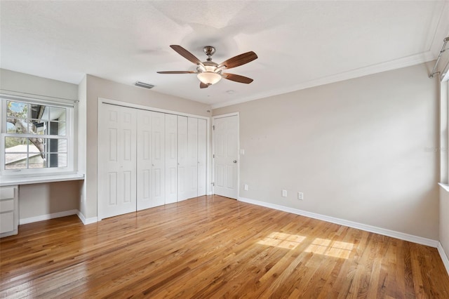 unfurnished bedroom featuring ceiling fan, crown molding, built in desk, and wood-type flooring