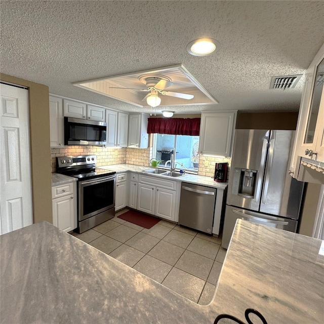 kitchen with light tile patterned flooring, sink, a raised ceiling, stainless steel appliances, and white cabinets