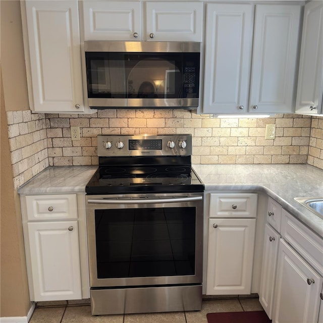 kitchen featuring tasteful backsplash, white cabinetry, appliances with stainless steel finishes, and light stone counters