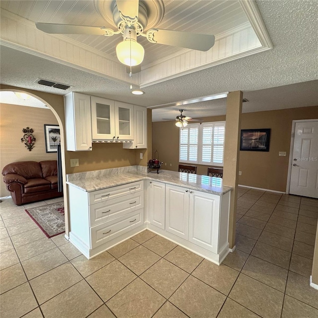 kitchen with light tile patterned flooring, kitchen peninsula, a raised ceiling, and white cabinets