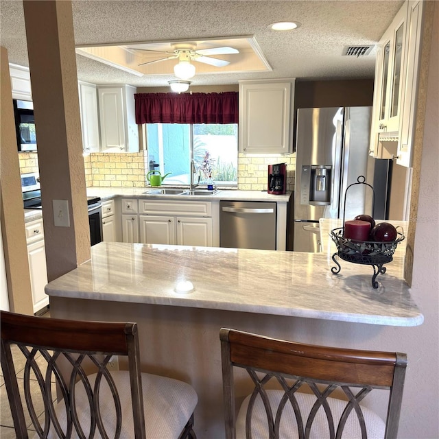 kitchen with sink, white cabinetry, a textured ceiling, appliances with stainless steel finishes, and a kitchen breakfast bar