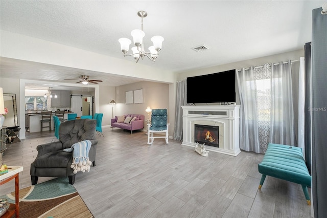 living room featuring ceiling fan with notable chandelier, light hardwood / wood-style floors, and a textured ceiling