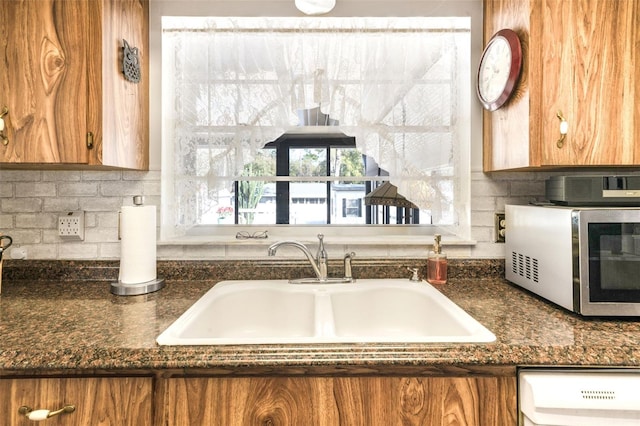 kitchen with dishwashing machine, sink, decorative backsplash, and dark stone counters