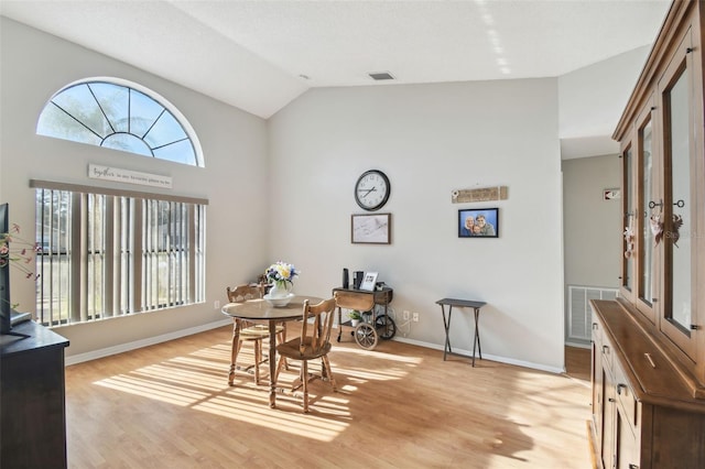 dining area with high vaulted ceiling and light hardwood / wood-style floors