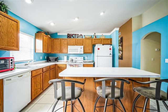 kitchen with white appliances, sink, a breakfast bar area, and light tile patterned floors