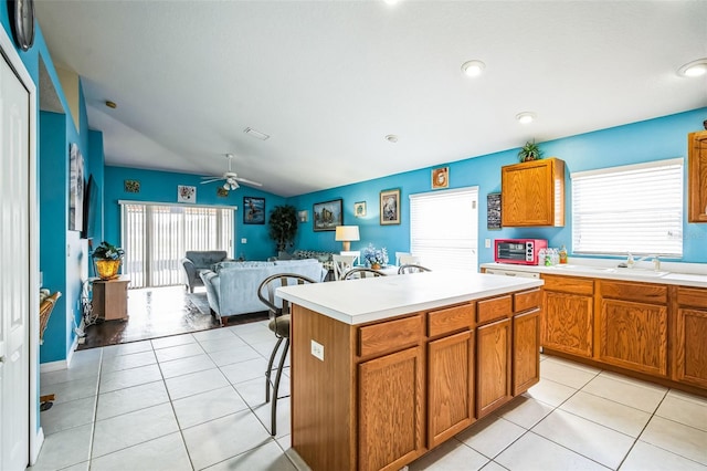 kitchen featuring vaulted ceiling, a breakfast bar, light tile patterned floors, ceiling fan, and a center island with sink