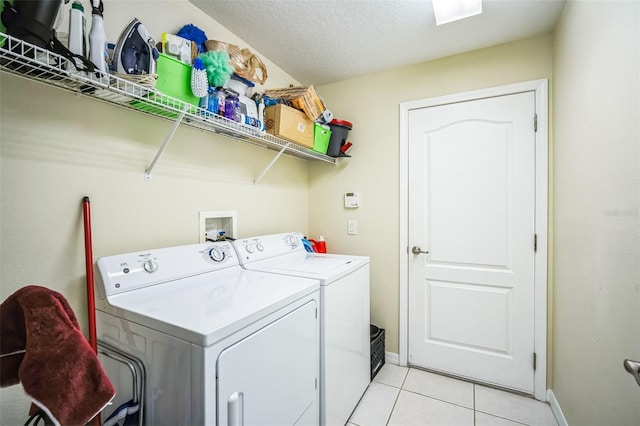 clothes washing area with washing machine and clothes dryer, a textured ceiling, and light tile patterned floors