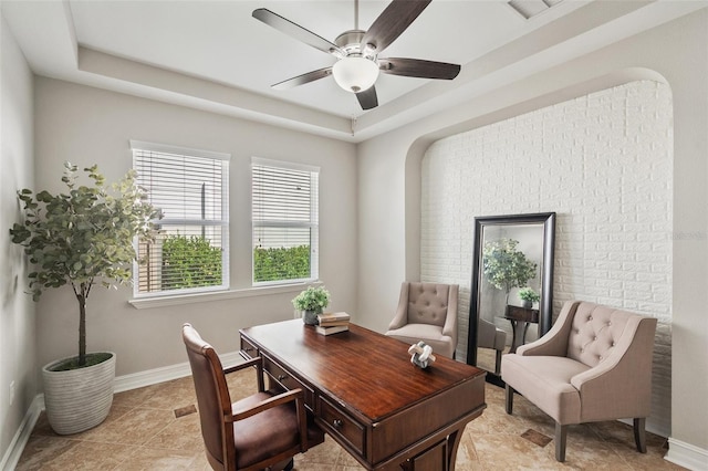 tiled office space featuring ceiling fan and a tray ceiling