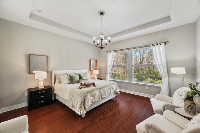 bedroom with dark wood-type flooring, a raised ceiling, and an inviting chandelier