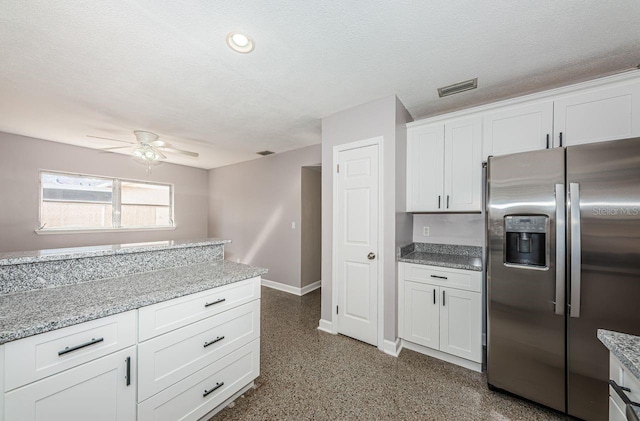 kitchen with white cabinetry, stainless steel fridge, light stone countertops, and a textured ceiling