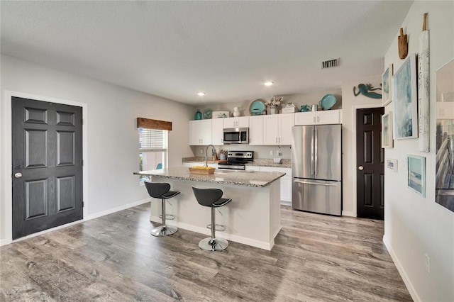 kitchen featuring a kitchen bar, white cabinetry, light stone counters, appliances with stainless steel finishes, and an island with sink