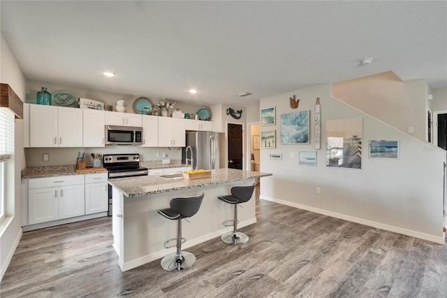 kitchen featuring sink, a breakfast bar, appliances with stainless steel finishes, white cabinetry, and a center island with sink