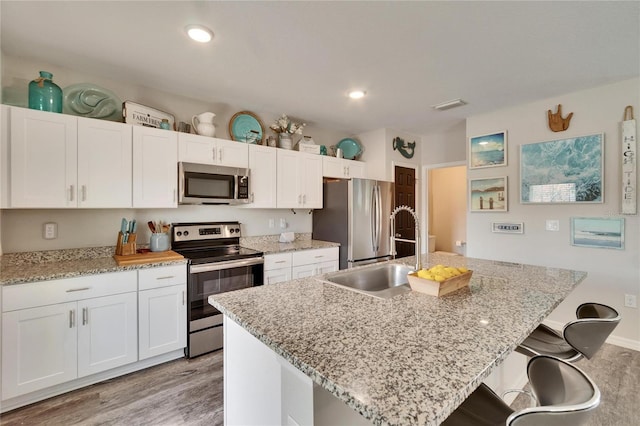 kitchen with sink, a breakfast bar area, appliances with stainless steel finishes, an island with sink, and white cabinets