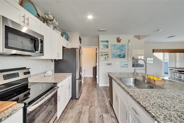 kitchen with appliances with stainless steel finishes, sink, white cabinets, light stone counters, and light hardwood / wood-style floors