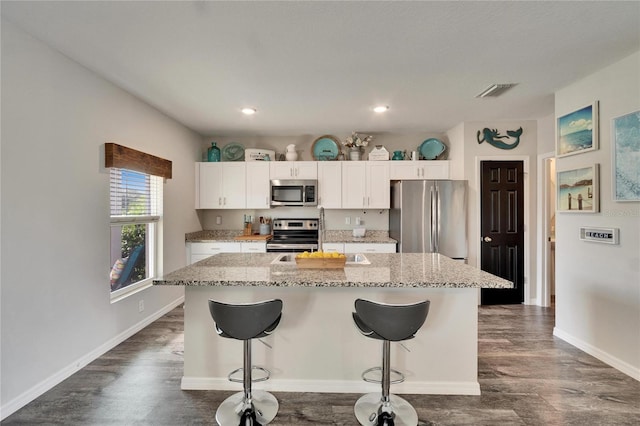 kitchen featuring white cabinetry, an island with sink, appliances with stainless steel finishes, and a kitchen bar