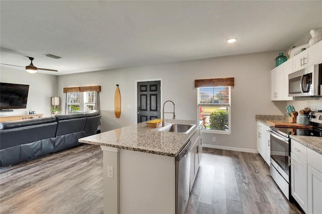 kitchen featuring sink, white cabinetry, light stone counters, a center island with sink, and stainless steel appliances