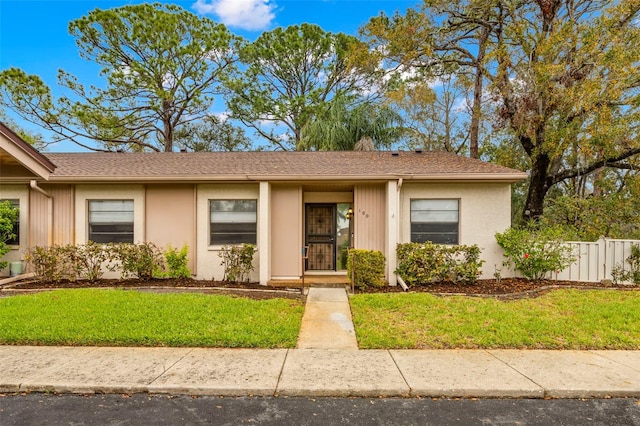 ranch-style home featuring roof with shingles, fence, a front lawn, and stucco siding