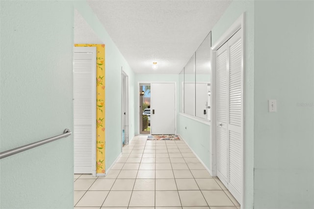 hallway featuring baseboards, a textured ceiling, and light tile patterned flooring