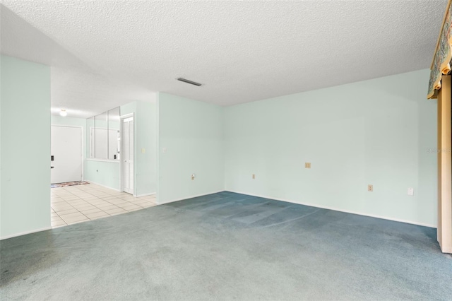 carpeted empty room with visible vents, a textured ceiling, and tile patterned floors