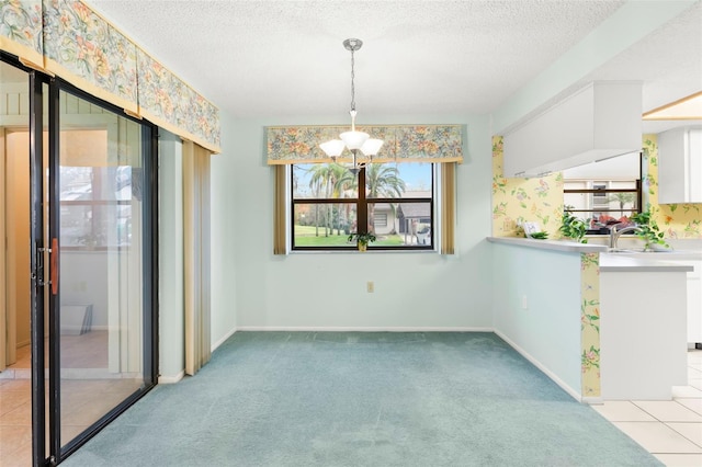 unfurnished dining area featuring a textured ceiling, baseboards, a notable chandelier, and light colored carpet