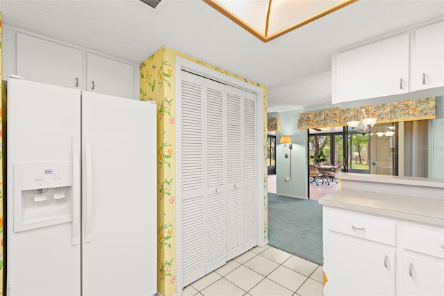 interior space with a chandelier, light tile patterned floors, white refrigerator with ice dispenser, white cabinets, and light countertops