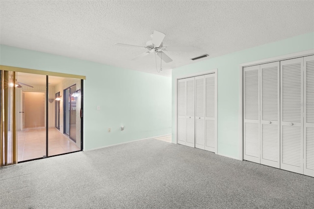 unfurnished bedroom with a textured ceiling, ceiling fan, carpet floors, visible vents, and two closets