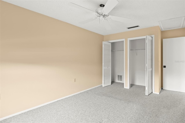 unfurnished bedroom featuring carpet, two closets, visible vents, and attic access