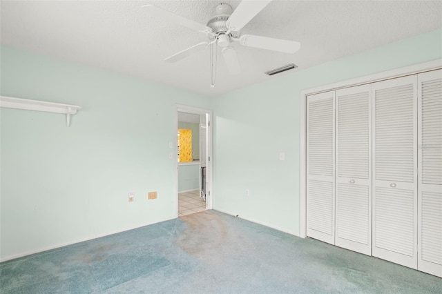 unfurnished bedroom with a textured ceiling, carpet flooring, visible vents, a ceiling fan, and a closet