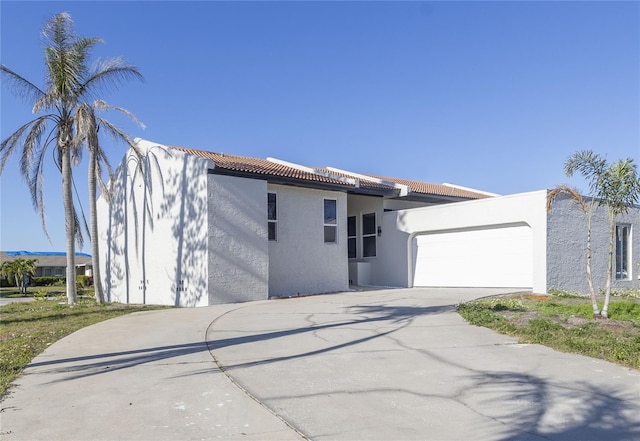 view of front of property featuring concrete driveway, a tile roof, an attached garage, and stucco siding