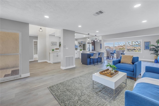 living room with a textured ceiling, baseboards, visible vents, and light wood-style floors