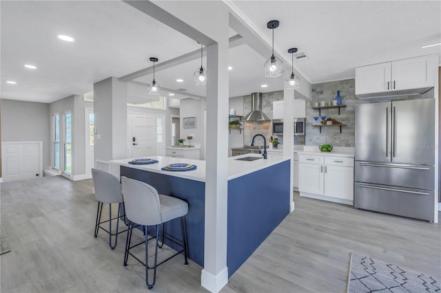 kitchen featuring stainless steel appliances, wall chimney range hood, light countertops, and white cabinetry