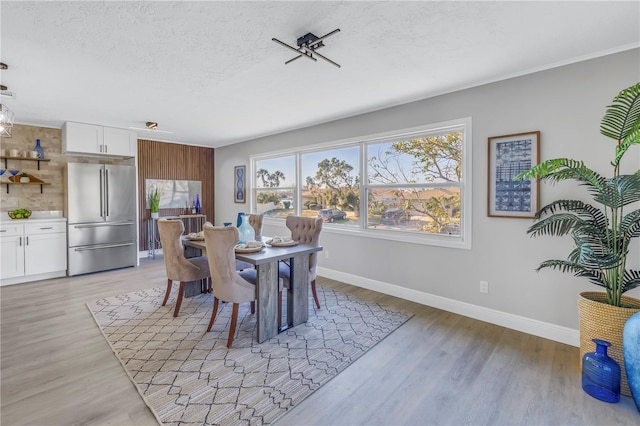 dining area with light wood-type flooring, a textured ceiling, and baseboards