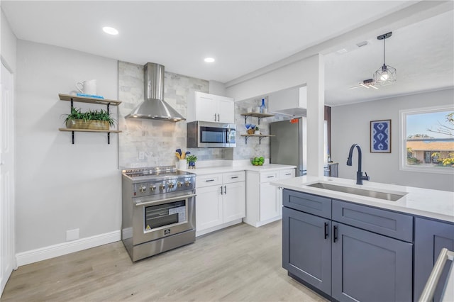 kitchen with stainless steel appliances, light countertops, white cabinets, a sink, and wall chimney range hood